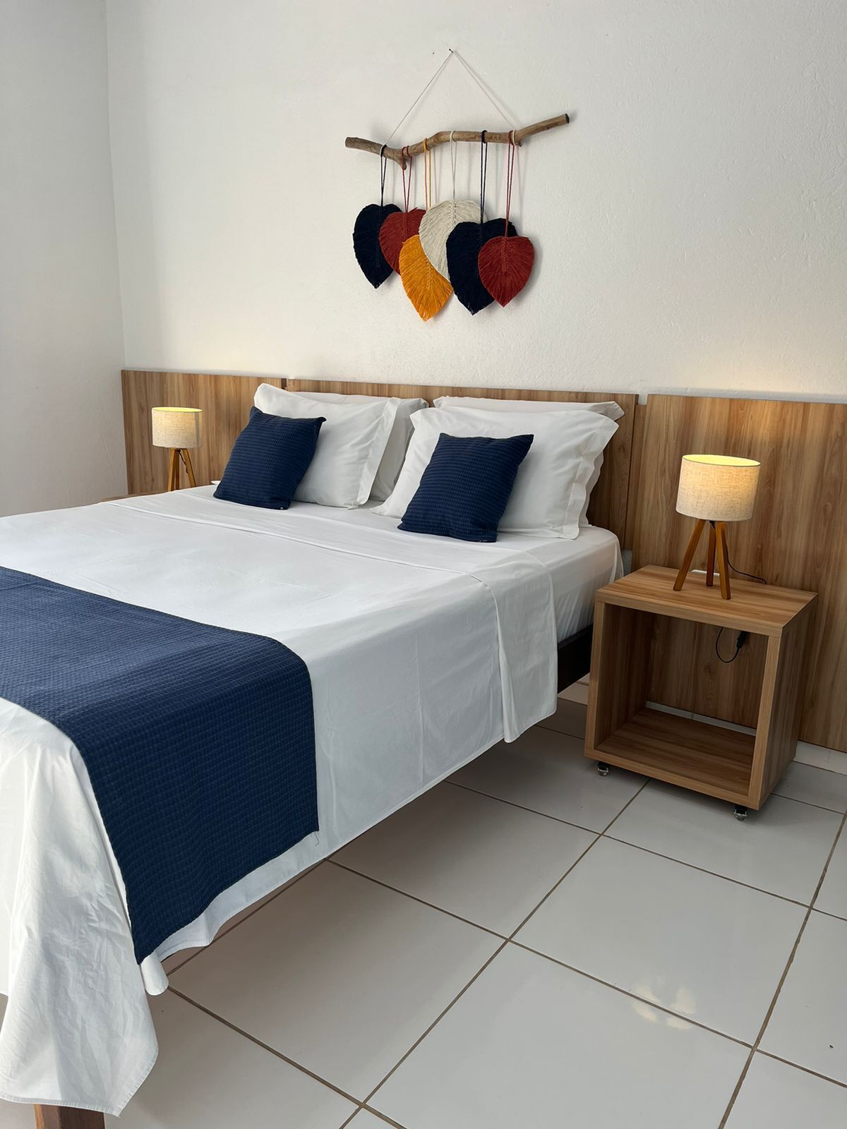 A neatly made bed with white and blue bedding, two bedside tables with lamps, and a wall-mounted heart decoration.
