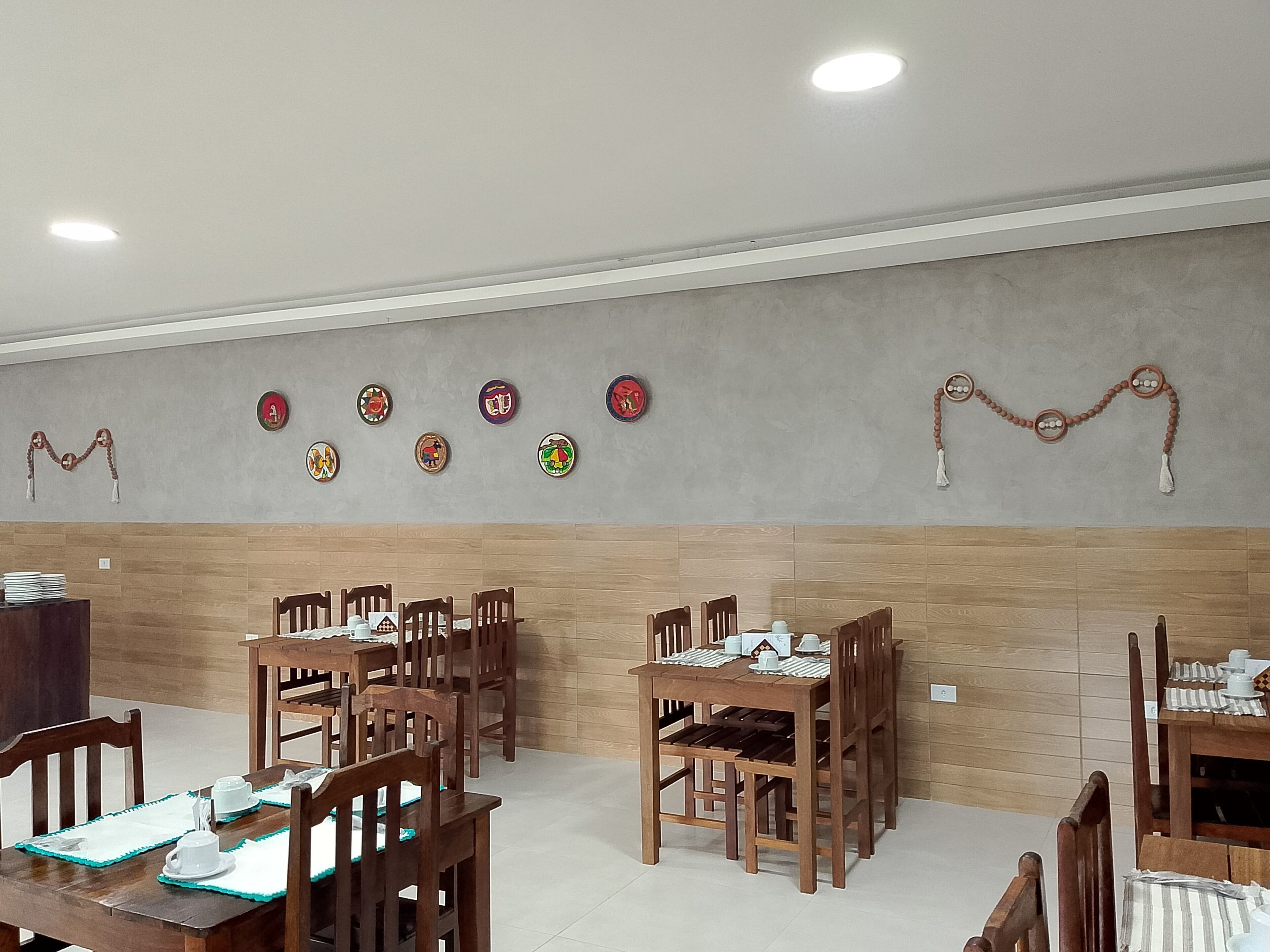 Un comedor con mesas y sillas de madera, una pared decorada con platos y un techo con iluminación empotrada.
