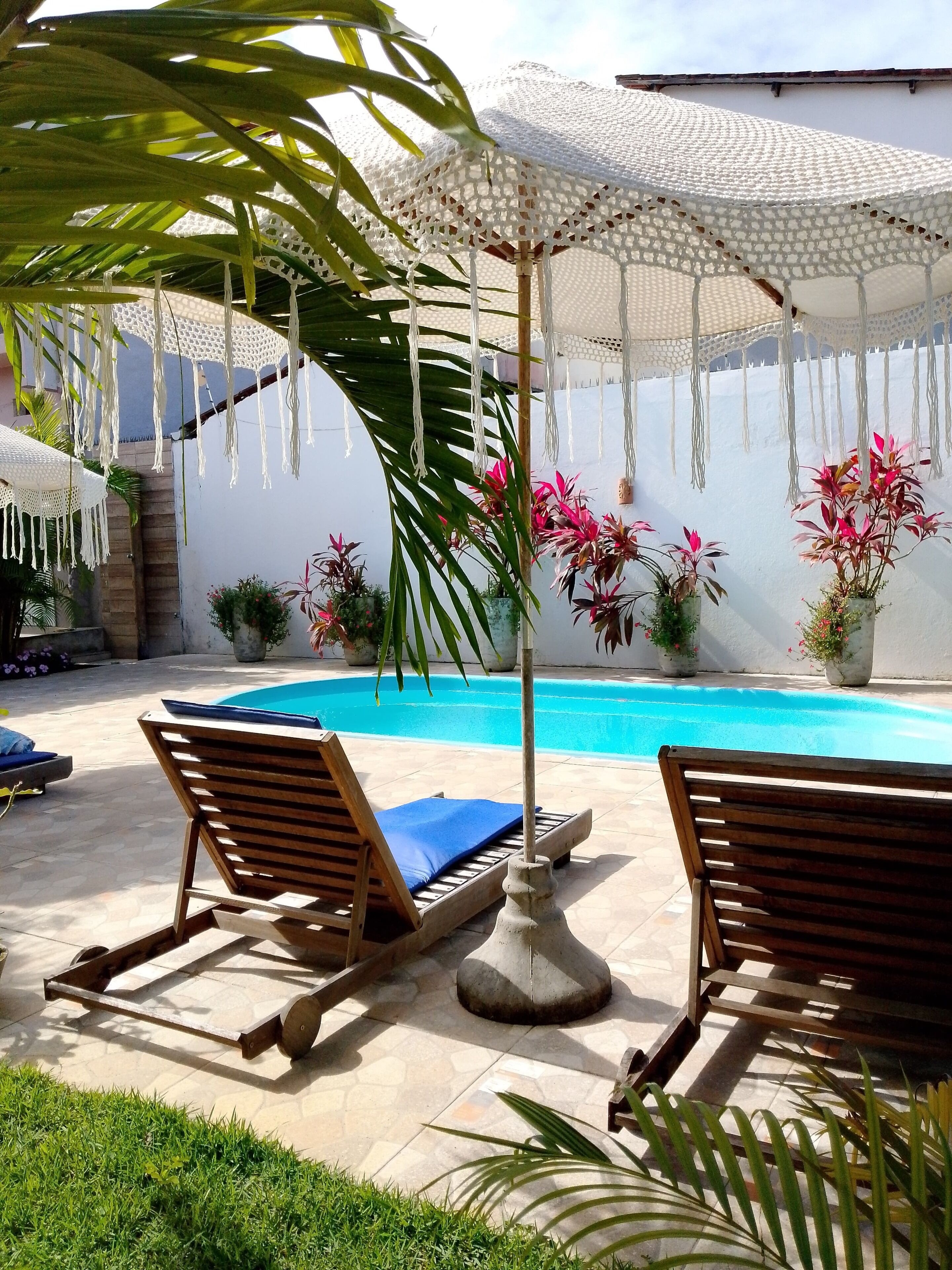 A poolside area with two wooden lounge chairs, a white umbrella, and potted plants.