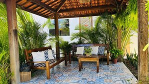 A covered outdoor seating area with a tiled floor, wooden furniture, and potted plants. - Pousada Maresia (São Miguel dos Milagres)