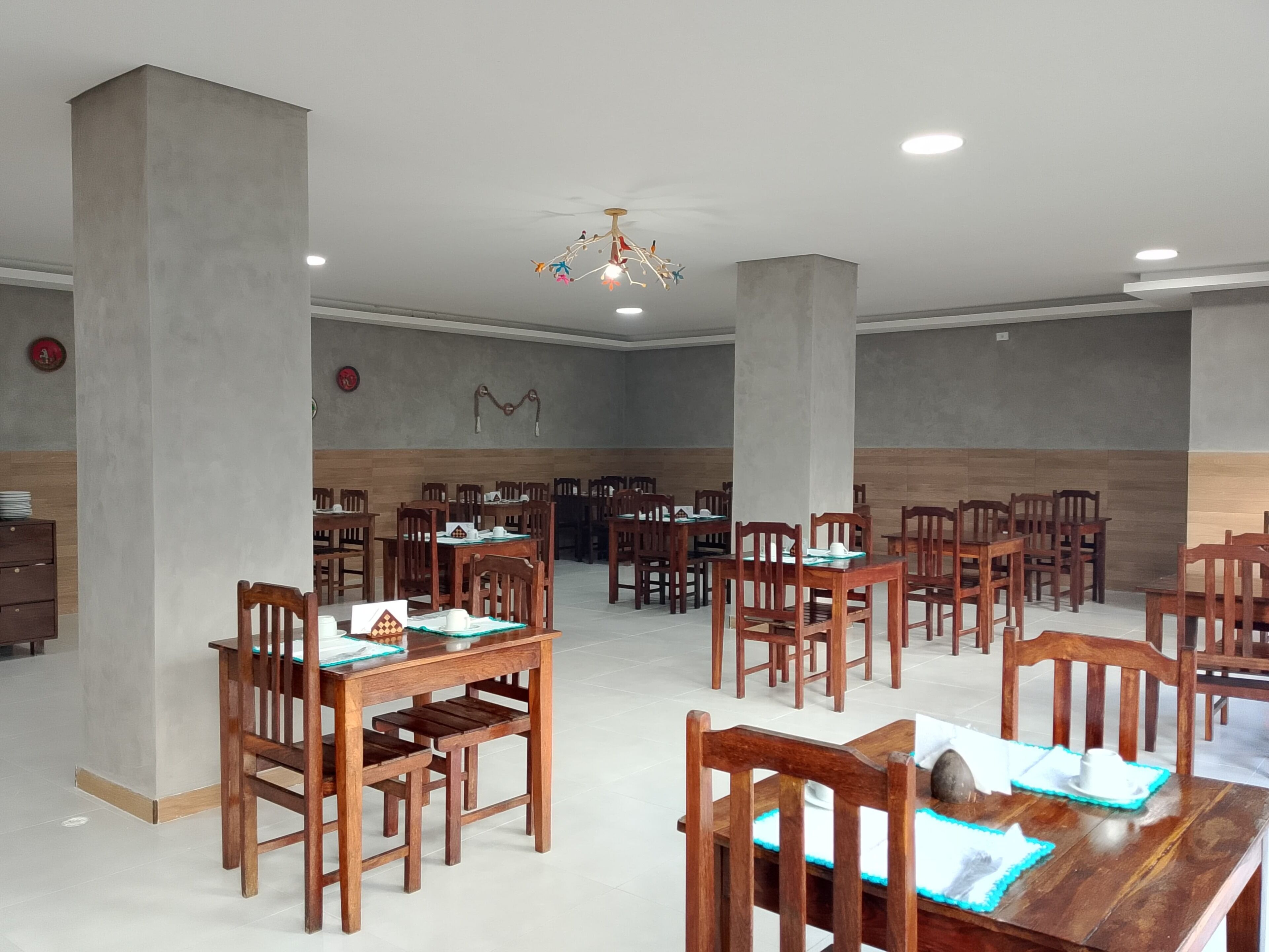 A spacious dining area with multiple wooden tables and chairs, a chandelier, and a tiled floor.
