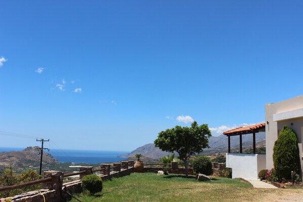 Une vue sur la côte, avec une maison, un ciel dégagé et des montagnes à l’horizon.