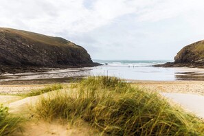 A coastal beach with grassy dunes and rocky cliffs.