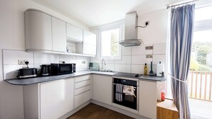 A modern kitchen with white cabinets, a built-in oven, and a window with curtains. - Luxury chalet in wonderful Pembrokeshire National Park, beach & coast path (Nolton Haven)