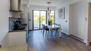 A modern kitchen with a built-in stove, a dining area with a table and chairs, and a large sliding glass door leading to a balcony. - Brand New Two Br Penthouse With a Private Roof Patio! Totally Equipped (Tulum)