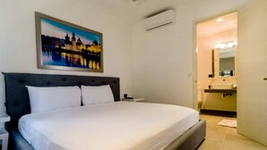A hotel room with a large bed, a nightstand, a wall-mounted air conditioner, and a painting of a cityscape. - Brand New Two Br Penthouse With a Private Roof Patio! Totally Equipped (Tulum)