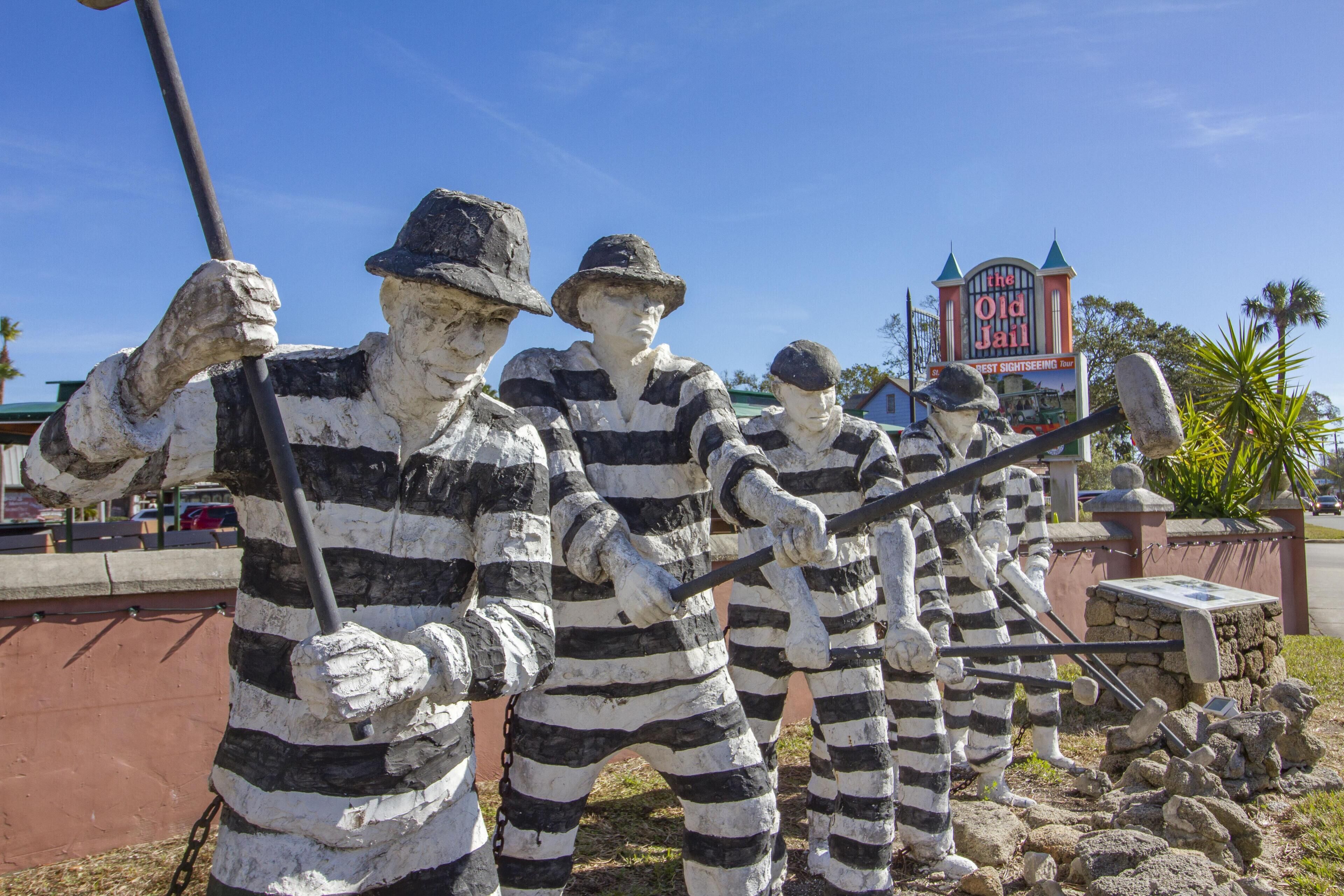 Un grupo de estatuas a rayas en un parque, con un cartel al fondo que dice "The Old Jail".