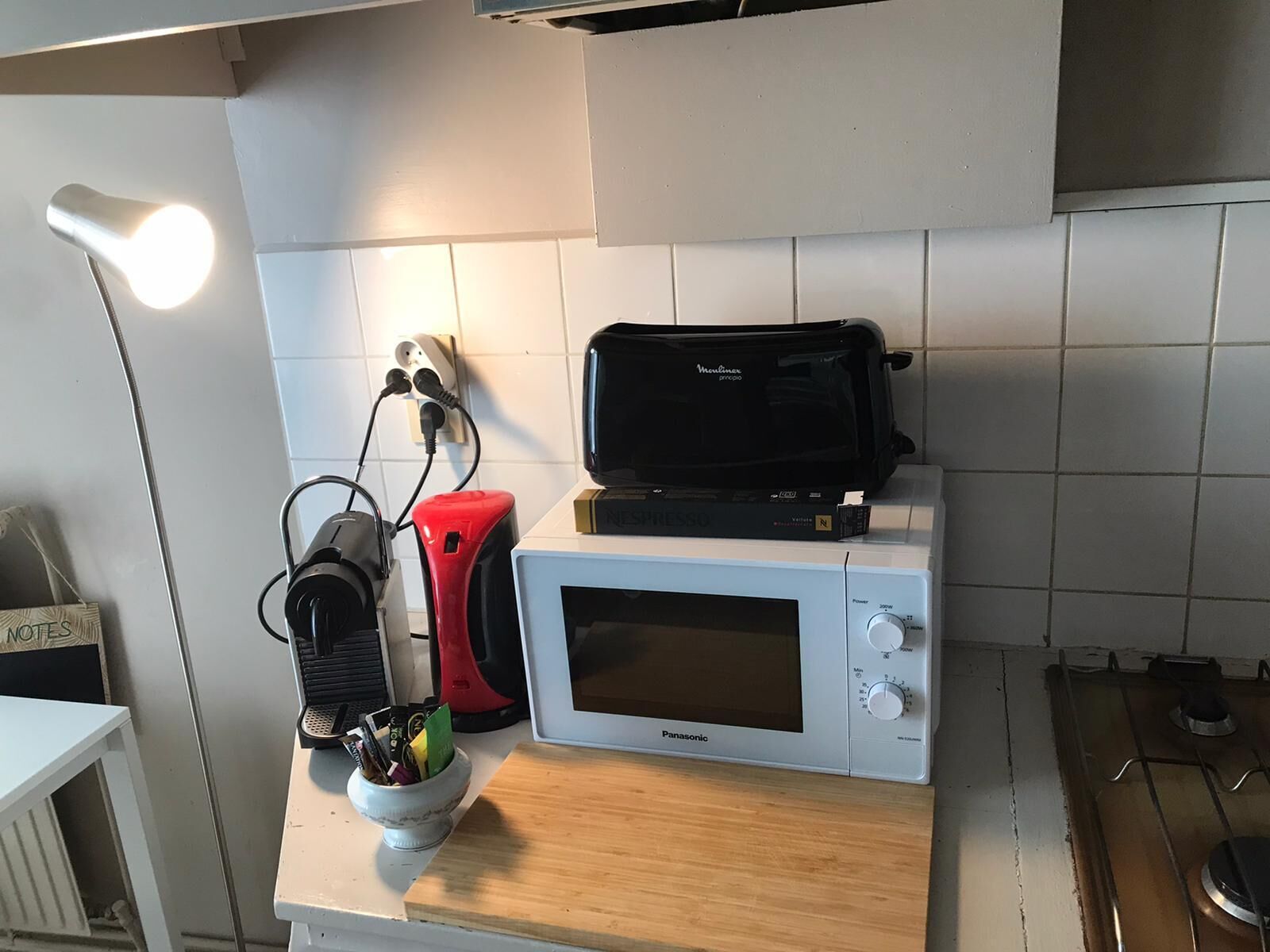 A kitchen with a microwave, toaster, kettle, and a bowl of items on the counter.