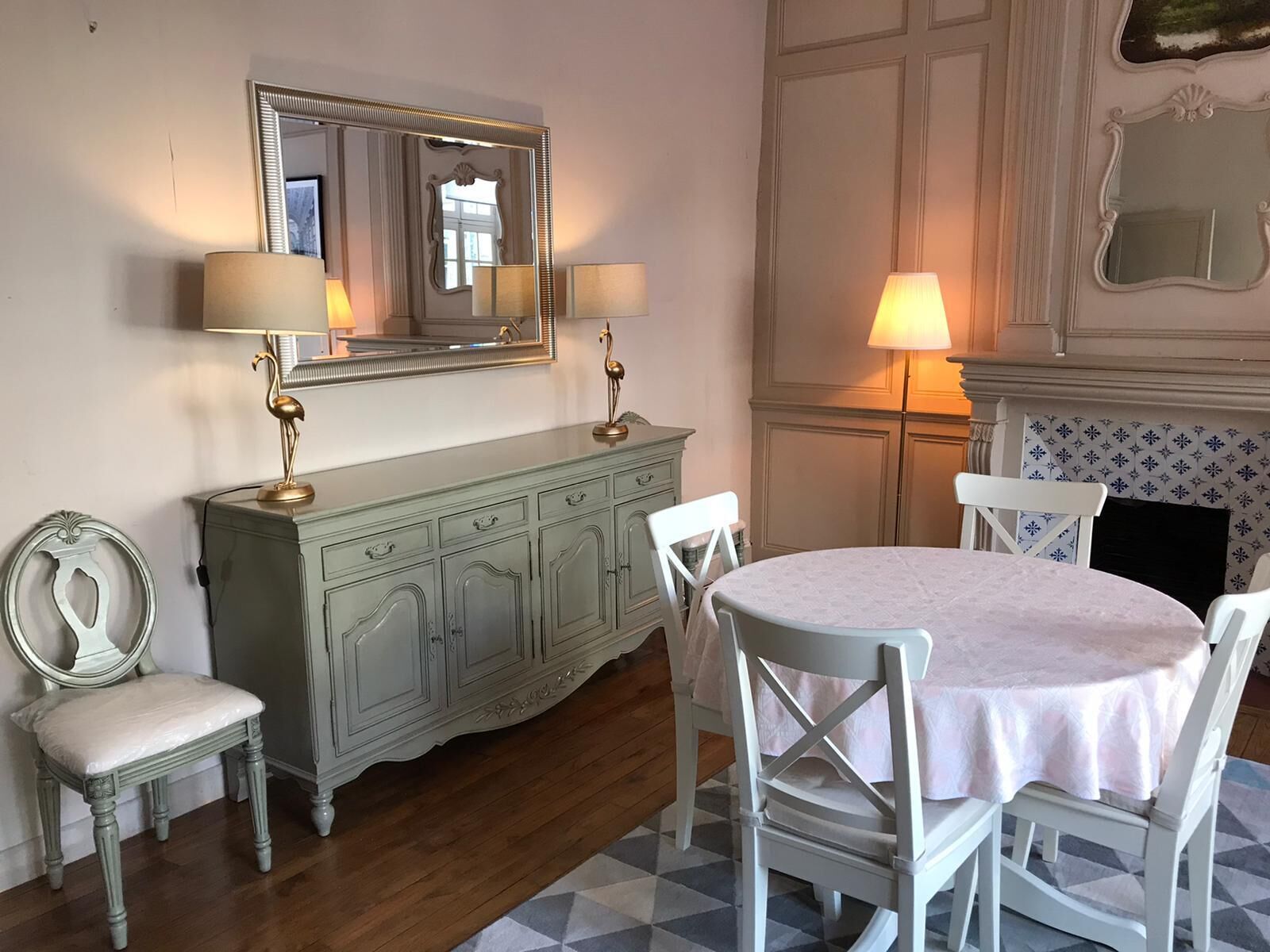 Een eetkamer met een witte ronde tafel, twee stoelen, een lichtgroene kast en twee wandlampen.