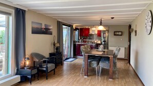A cozy living room with a dining area, a kitchen in the background, and a large window with curtains. - Holiday Home With Winter Garden by the Lauwersmeer for 4 Guest (Anjum)