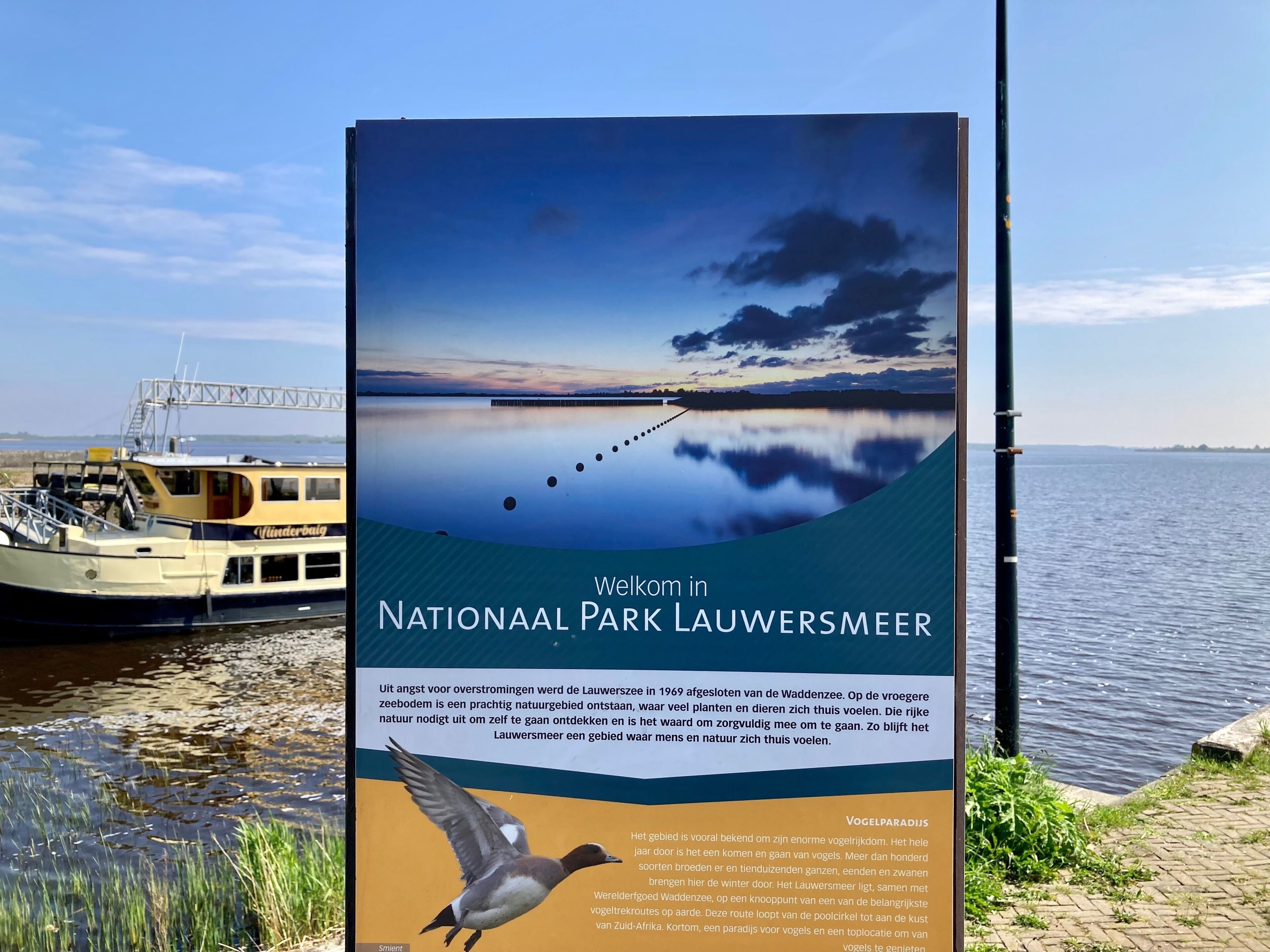A sign for the National Park Lauwersmeer with a boat and calm water in the background.