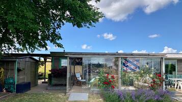 A glass-enclosed building with a patio area, surrounded by a garden with red and purple flowers.