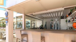 An outdoor bar area with wicker bar stools, a counter, hanging wine glasses, and shelves with bottles and plants. - Parque nº 8 - Two Bedroom Penthouse Apartment (Ferragudo)