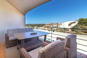 A balcony with wicker furniture, a table, and a view of a coastal town.