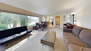 A modern living room with a sofa, a coffee table, and a dining area with chairs and a table. - Private Beach House with amazing views of Shwan Lake and Twin Lakes Beach (Santa Cruz)