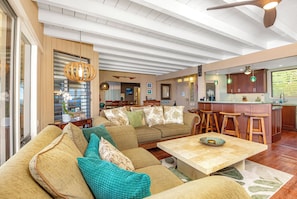 Uma sala de estar espaçosa com um sofá grande, uma mesa de centro e uma área de cozinha com banquetas de bar.