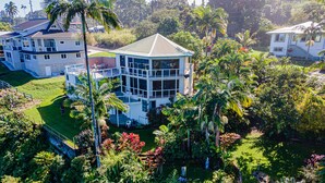 A large, multi-story house surrounded by lush tropical vegetation. - Paradise Bluff: Cliffside Home w/Gorgeous Ocean Views and Tropical Garden (Laupahoehoe)