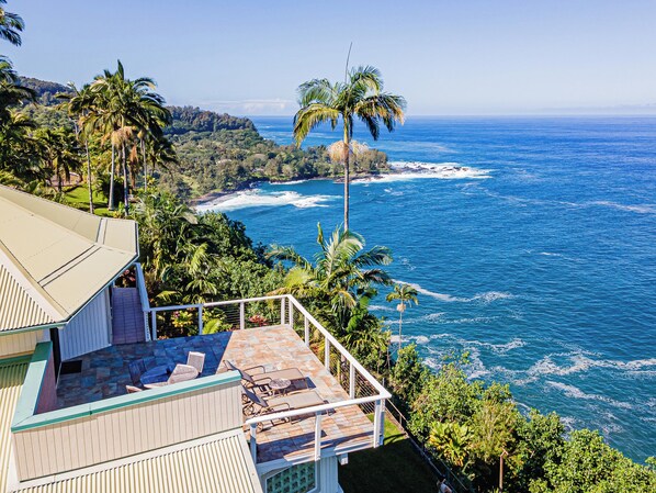 A coastal property with a patio overlooking the ocean, surrounded by lush greenery and palm trees.