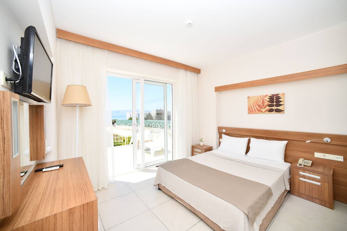 A hotel room with a bed, a TV, a desk, and a view of the outdoors.