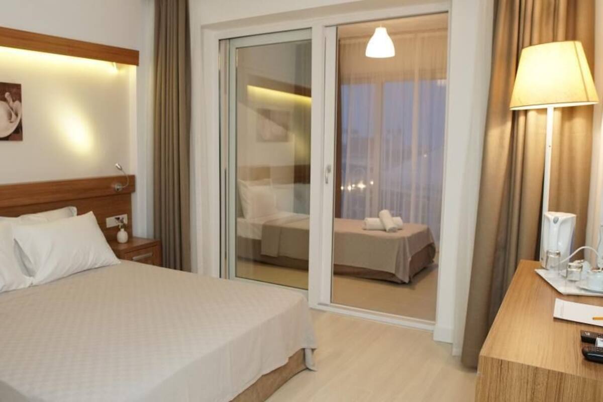 A hotel room with a bed, a desk with a lamp, and a sliding glass door leading to a balcony.