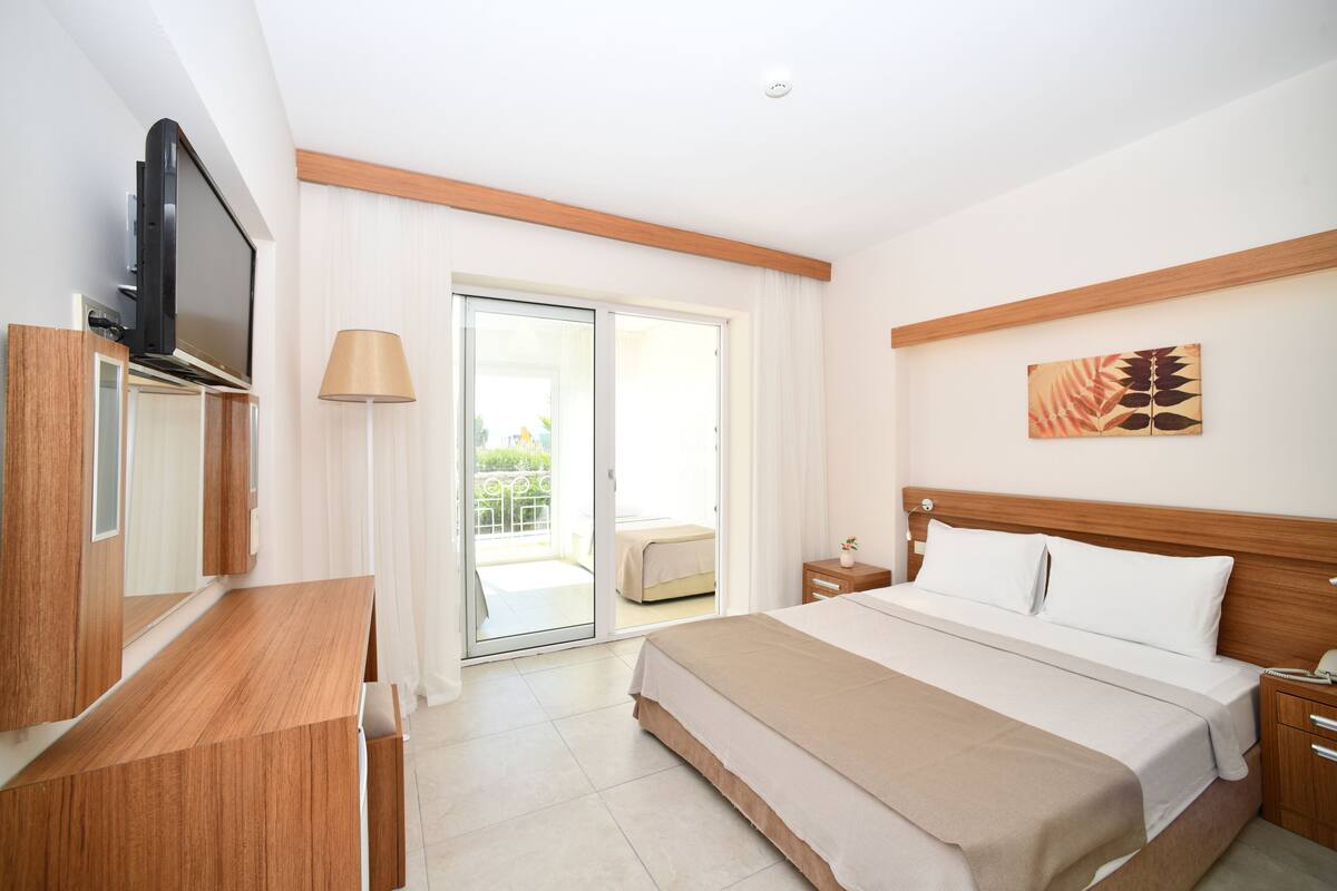 A hotel room with a bed, a TV, a desk, a lamp, and a sliding glass door to a balcony.