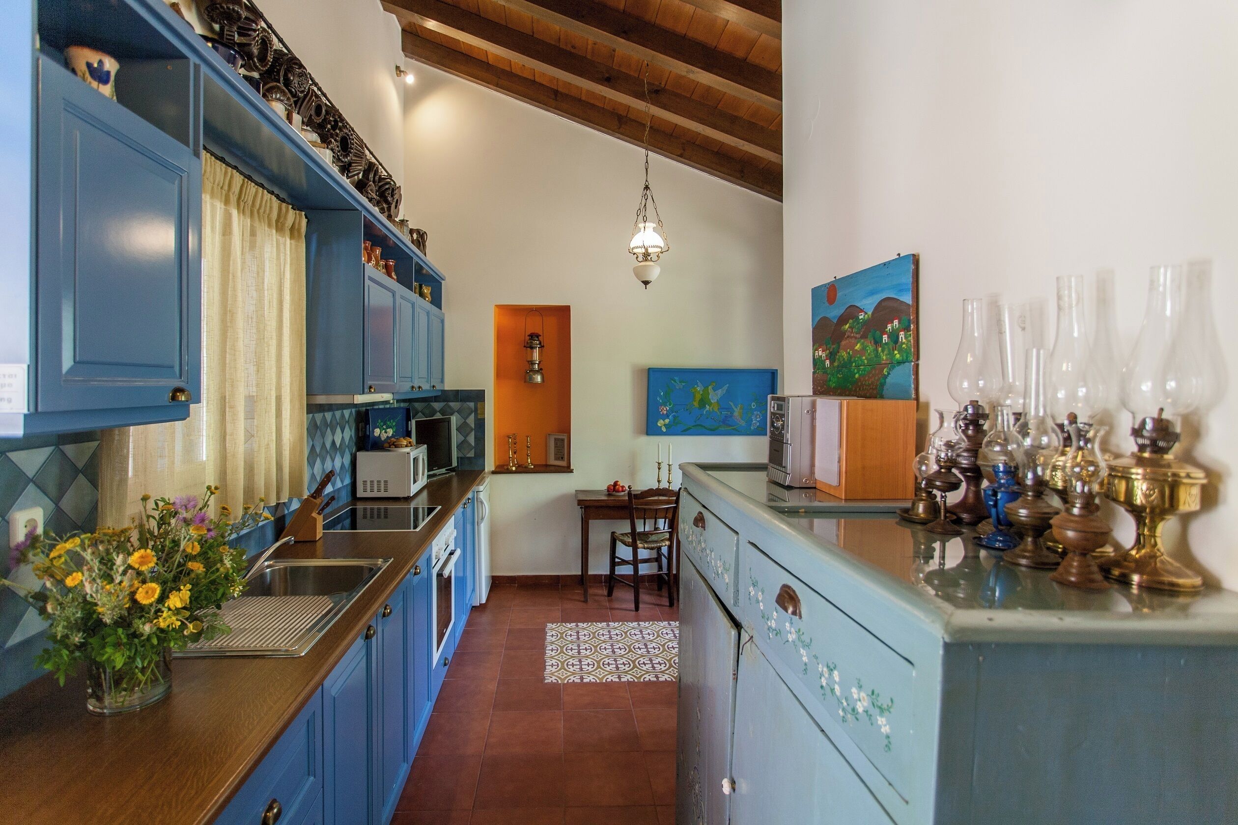 Une cuisine avec des meubles de rangement bleus, un coin repas avec une table et des chaises, et un luminaire suspendu.