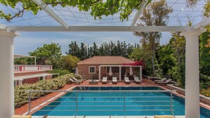 A swimming pool with lounge chairs and a pergola, surrounded by greenery and a brick building. - Dine on the Generous Veranda at a Rustic Stone Getaway (Platanias)