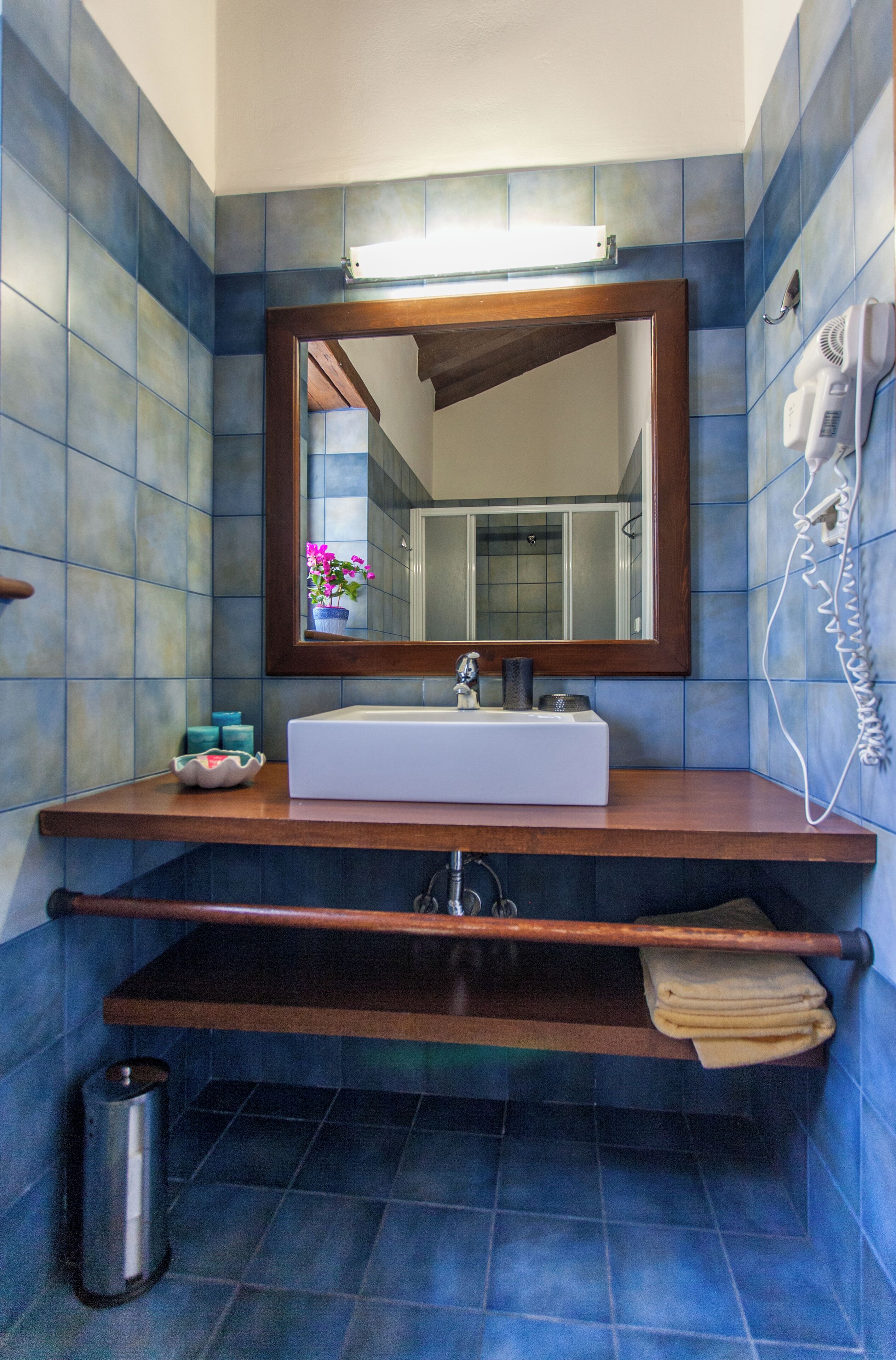 Ein Badezimmer mit einem weißen Waschbecken, einer Holz-Kommode, einem Spiegel und einem an der Wand befestigten Fön.