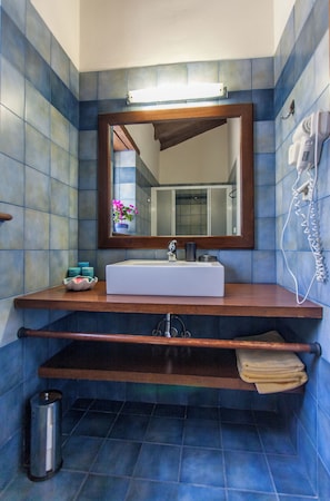 A bathroom with a white sink, a wooden vanity, a mirror, and a hairdryer on the wall.