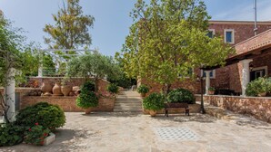 A stone-paved courtyard with steps leading to a building, surrounded by potted plants and a tree. - Dine on the Generous Veranda at a Rustic Stone Getaway (Platanias)