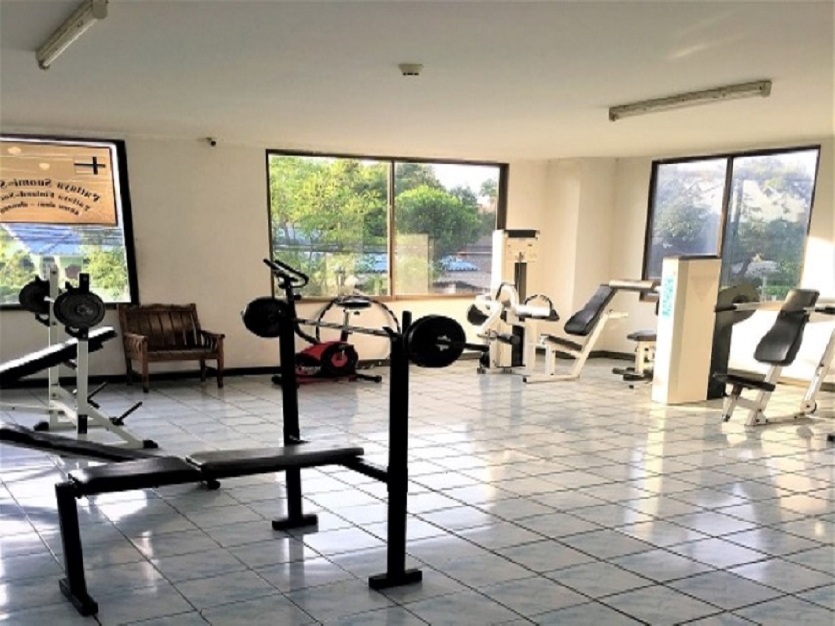 Ein Fitnessstudio mit unterschiedlichen Trainingsgeräten, großen Fenstern und einem gefliesten Boden.