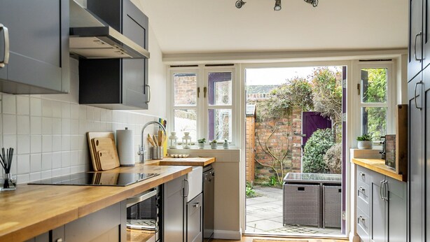 A modern kitchen with a wooden countertop, stainless steel appliances, and a view of a garden through an open door. - 3 Darnborough Street -  a family break that sleeps 4 guests  in 2 bedrooms (York)