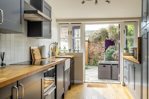 Una cocina moderna con encimera de madera, electrodomésticos de acero inoxidable y vistas a un jardín a través de un ventanal abierto.