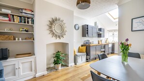A modern kitchen with grey cabinets, a dining area with a table and chairs, and a bookshelf filled with books. - 3 Darnborough Street -  a family break that sleeps 4 guests  in 2 bedrooms (York)
