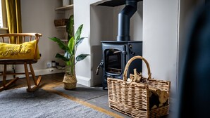 A cozy living room with a rocking chair, a potted plant, a fireplace, and a wicker basket with logs. - 3 Darnborough Street -  a family break that sleeps 4 guests  in 2 bedrooms (York)