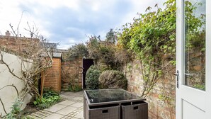 A patio area with a glass-top table and wicker furniture, surrounded by brick walls and greenery. - 3 Darnborough Street -  a family break that sleeps 4 guests  in 2 bedrooms (York)