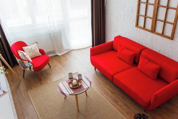 A living room with a red sofa, a red armchair, and a small table with two cups and a decorative item. - Apartment - Cismigiu Gardens (Bucharest)