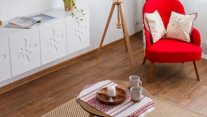 A modern living room with a flat-screen TV, a red armchair, a floor lamp, and a small table with a tray and candles. - Apartment - Cismigiu Gardens (Bucharest)