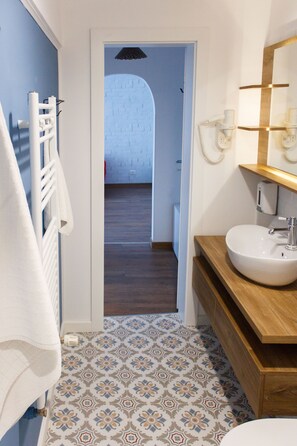 A bathroom with patterned floor tiles, a white towel rack, a wooden vanity with a sink, and a mirror with wall-mounted lights. - Apartment - Cismigiu Gardens (Bucharest)
