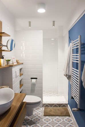 Ein modernes Badezimmer mit weißen Fliesen, einem Holzwaschtisch, einer Toilette, einer Duschkabine und einem Handtuchhalter.