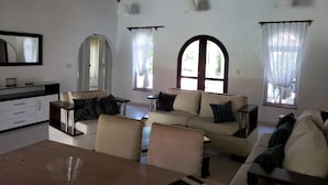 A spacious living room with a high ceiling, a sofa set, a dining table, and a kitchen area. - Villa 6 Bedrooms Guests Friendly (Sosúa)