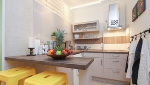 Cocina compacta con una isla central, taburetes amarillos y un frutero.