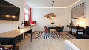Un espacio habitable moderno y funcional con zona de comedor, un televisor de pantalla plana grande, un escritorio de madera y una cama.