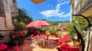 An outdoor patio with a table and chairs, a swing chair, and potted plants. - Central Spoleto Apartment With Large Sunny Terrace With Views (Spoleto)