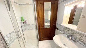 A bathroom with a glass shower enclosure, a wooden door, a sink with a mirror, and patterned tiles. - Central Spoleto Apartment With Large Sunny Terrace With Views (Spoleto)