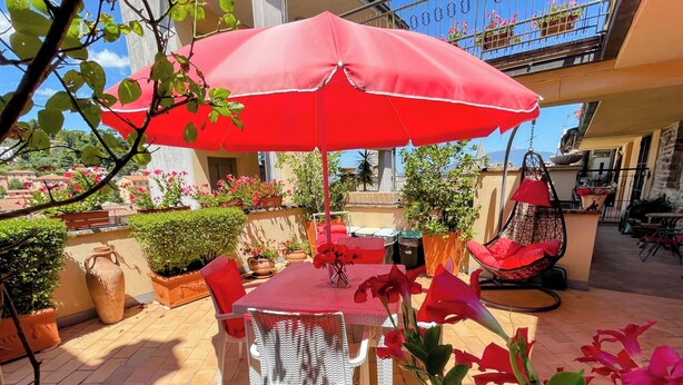 An outdoor patio with a red umbrella, wicker chairs, and potted plants. - Central Spoleto Apartment With Large Sunny Terrace With Views (Spoleto)
