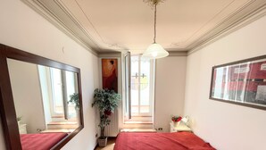 A hotel room with a large bed, a mirror, a potted plant, a small table with a lamp, and a window with a view. - Central Spoleto Apartment With Large Sunny Terrace With Views (Spoleto)