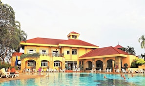 A large resort building with a swimming pool, multiple balconies, and outdoor seating areas.