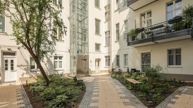 Ein Innenhof mit einem zentralen Weg, umgeben von Grünflächen und einem Gebäude mit zahlreichen Fenstern und Balkonen.