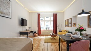 Ein Hotelzimmer mit Bett, Schreibtisch, Esstisch mit Stühlen, Fernseher und einem Fenster mit Vorhängen.
